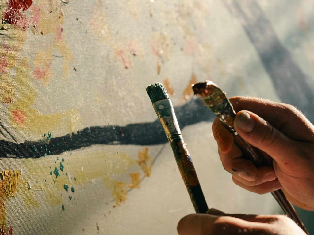 Hände malen gleichzeitig mit zwei Pinseln und Farbe auf eine Leinwand.