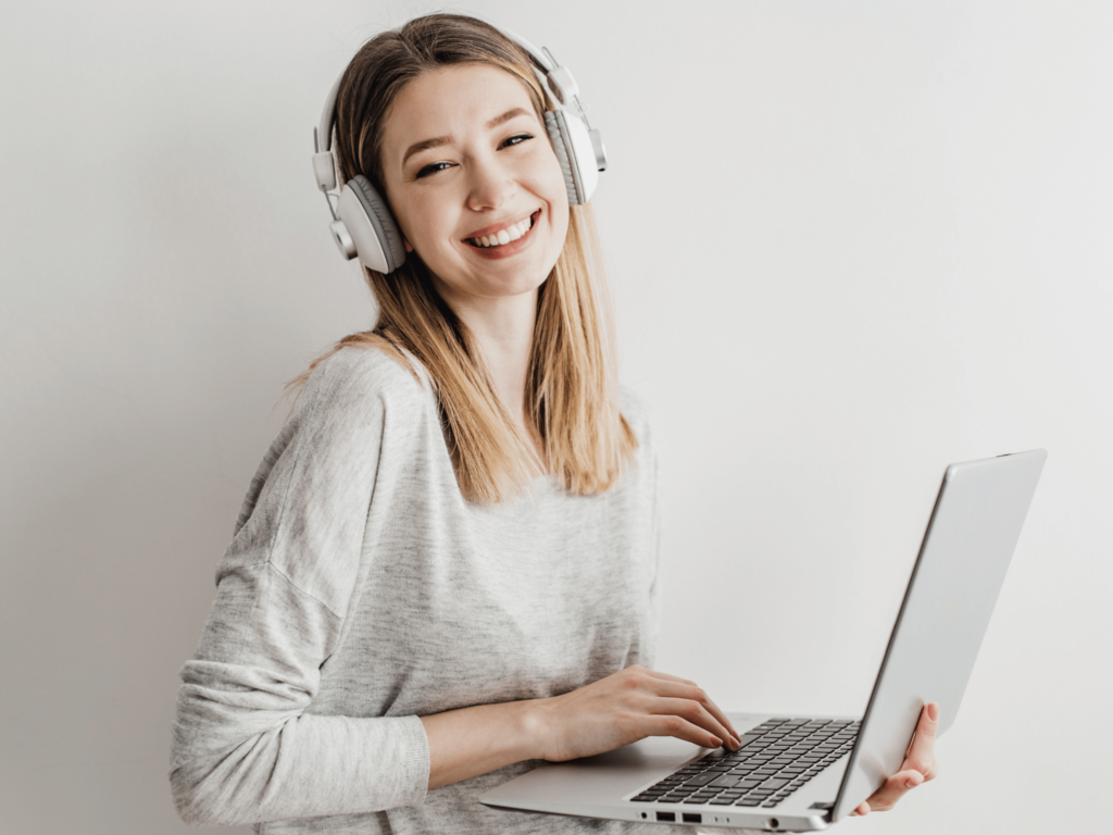 Ein Mädchen mit einem Laptop in der Hand und Kopfhörern auf den Ohren lächelt.