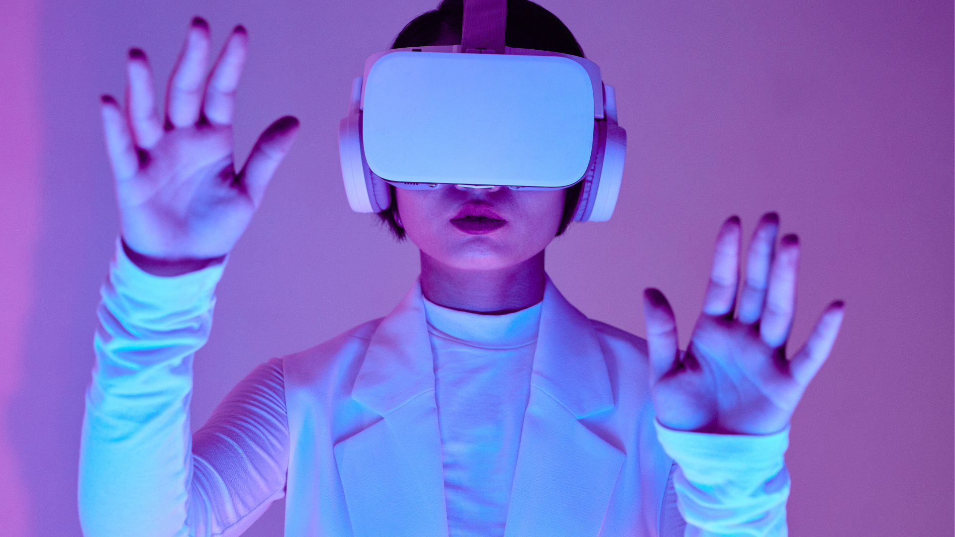 Person mit Virtual-Reality-Brille und Kopfhörern steht vor einem pink-blauen Hintergrund und hebt beide Hände, als würde sie eine digitale Umgebung steuern.