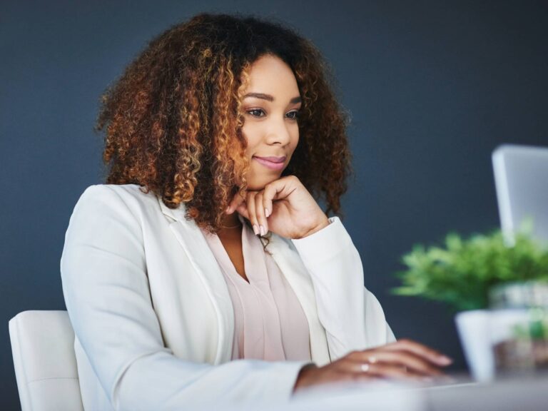 Elegante Frau sitzt vor dem Computer, stützt den Kopf und betrachtet den Bildschirm.