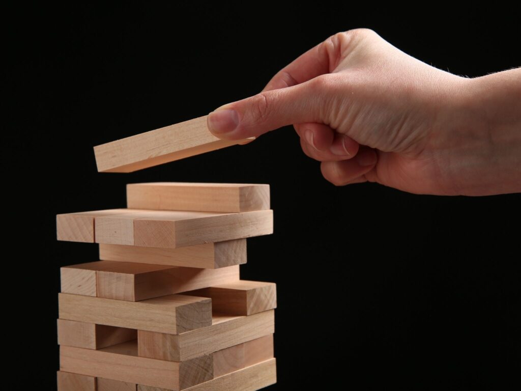 Hand stapelt einen Jenga-Holzblock auf einen wackeligen Turm.