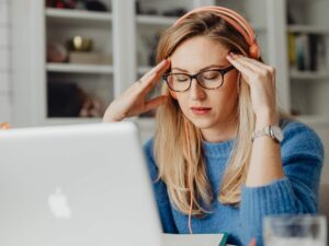 Frau sitzt vor einem Laptop und stützt den Kopf nachdenklich mit den Händen.