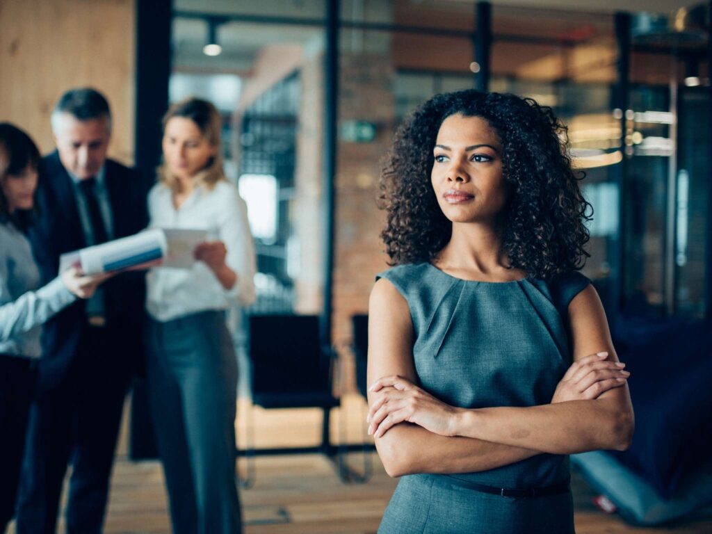 Mehrere Personen in einem Büro, eine Person steht vorne und denkt nach, während die Gruppe im Hintergrund diskutiert und analysiert.
