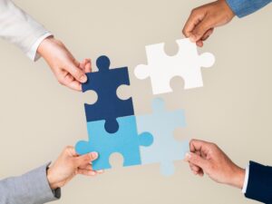 Vier Hände setzen vier Puzzleteile zu einem Ganzen zusammen – Teamarbeit, Kooperation und Kommunikation im Fokus.