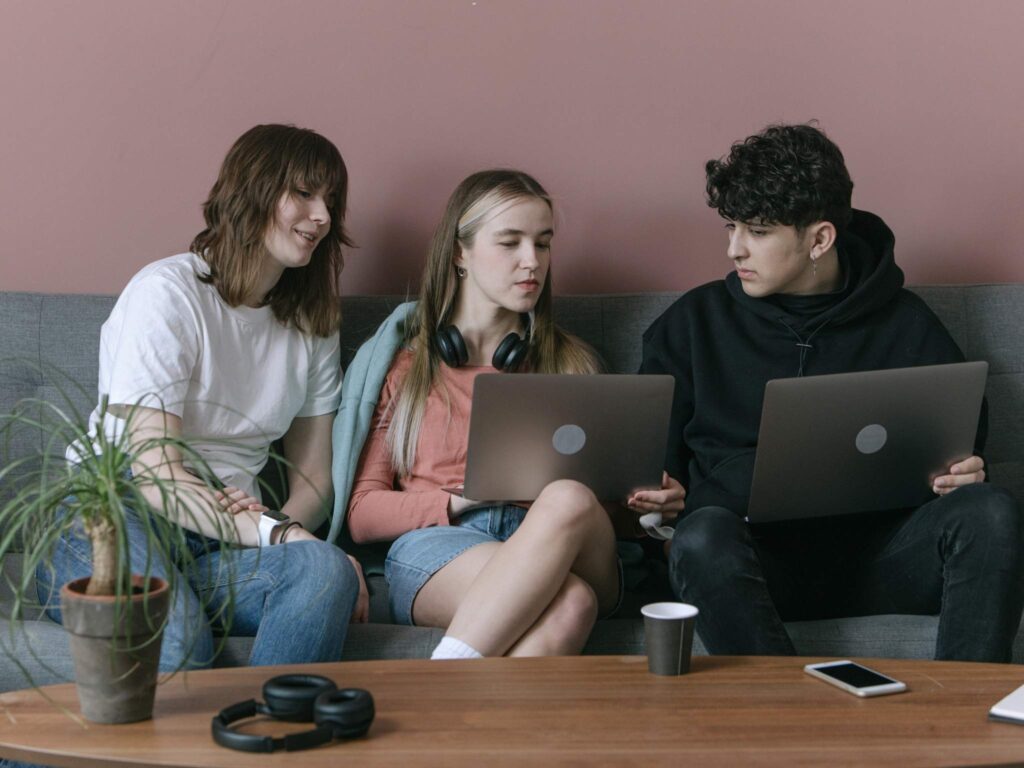 Jugendliche sitzen auf einer Couch, nutzen Laptops und diskutieren gemeinsam.