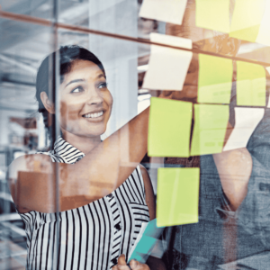 Person ordnet Haftnotizen an einer Glaswand, um Rückmeldungen zu strukturieren und Ergebnisse gemeinsam zu reflektieren.