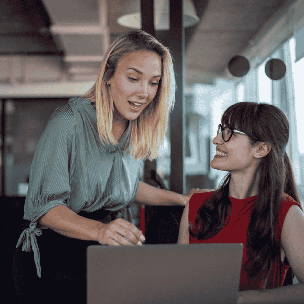 Zwei Personen sitzen vor einem Laptop und sprechen miteinander in einer Feedback- oder Coaching-Situation.