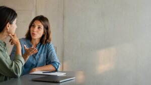 Zwei Frauen im Gespräch. Eine Frau spricht und gestikuliert mit der Hand, die andere hört aufmerksam zu. Die Szene steht für Satzakzent, Intonation und Bedeutungsfokus im Gespräch.
