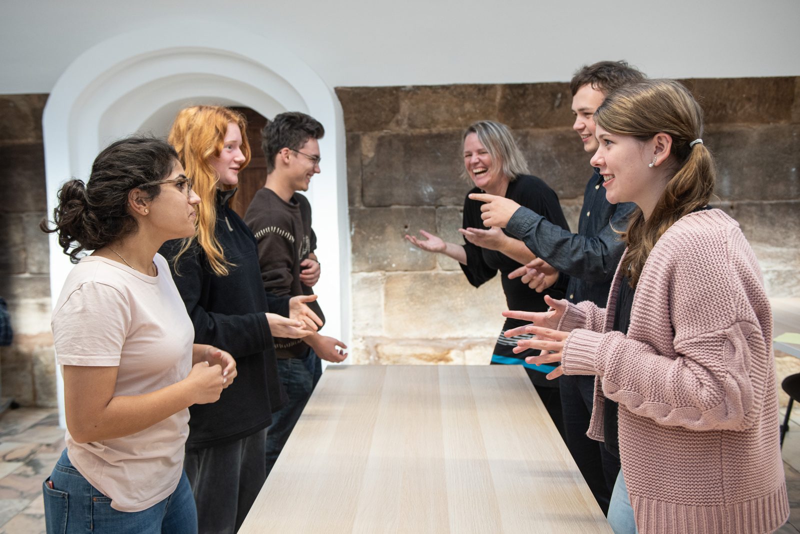 Claudia Böschel lacht mit einer Gruppe bei einer Gesten-Übung am Tisch