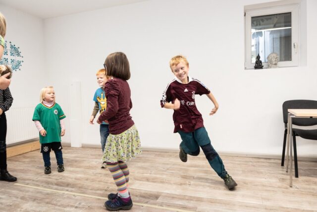 Kinder rennen und lachen bei einem Bewegungsspiel im Kursraum